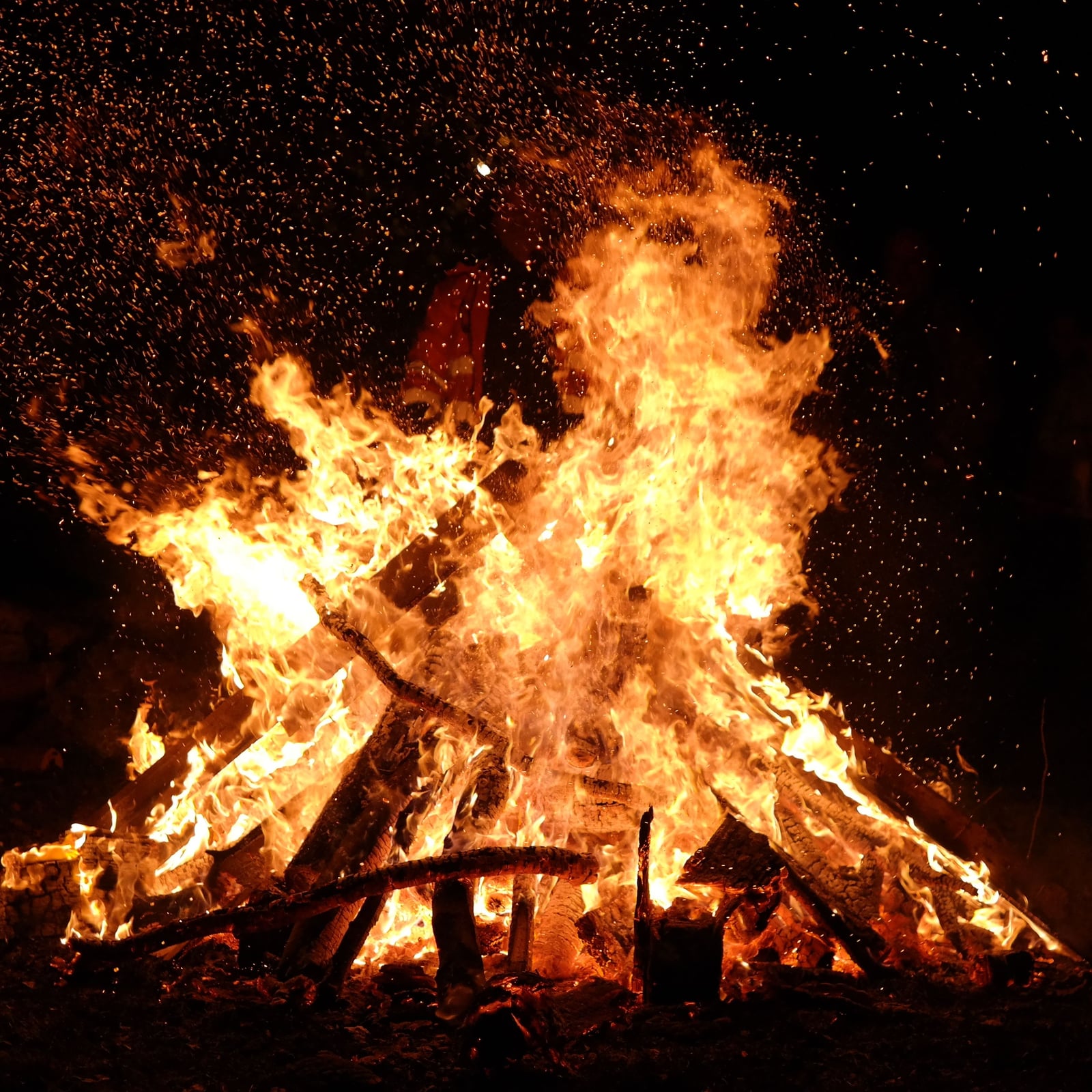 Een groot kampvuur in het donker, met vonken die opstijgen in de nacht