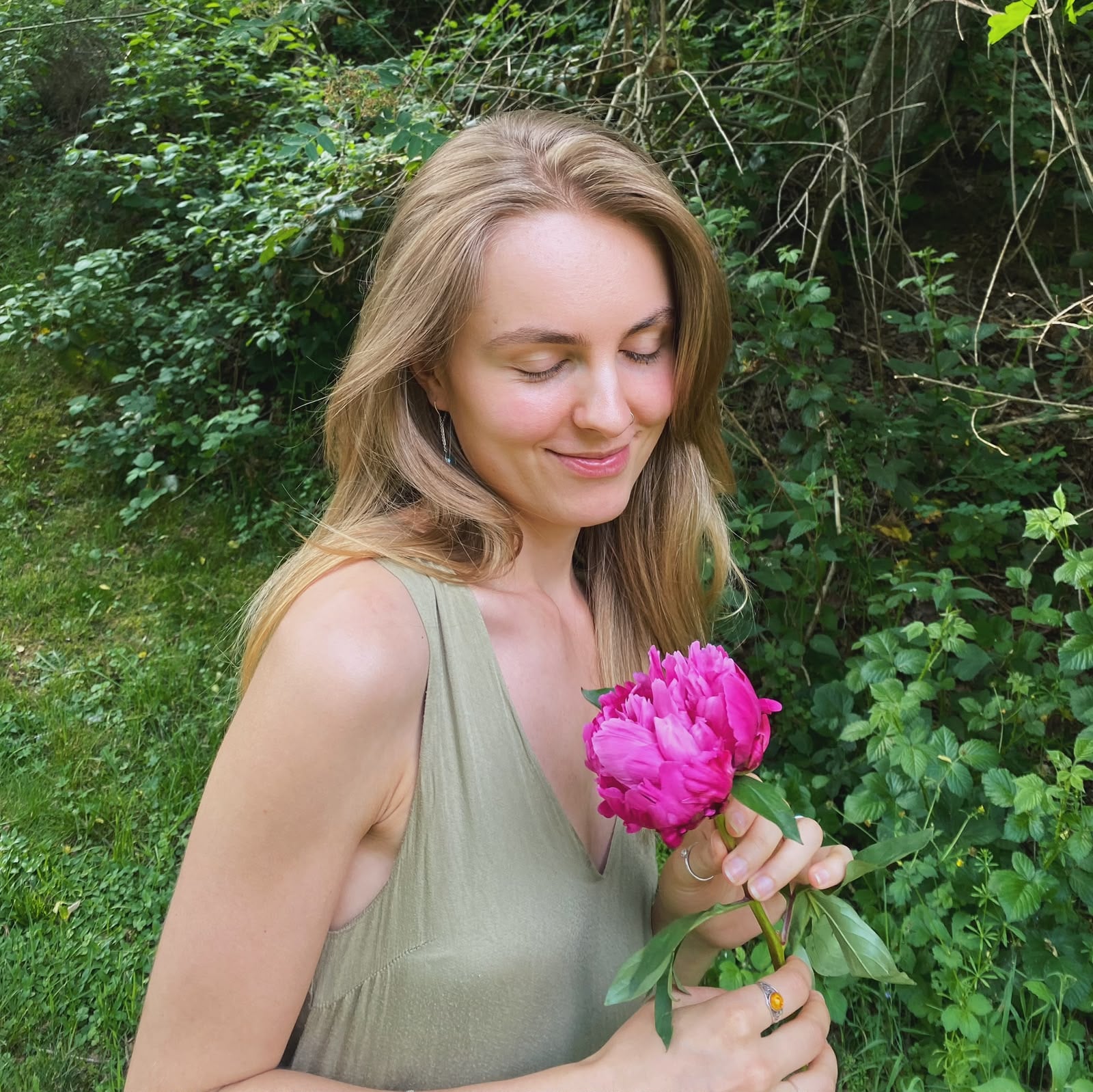 Vrouw in de tuin met een roze pioenroos, symbool voor zachtheid en rust