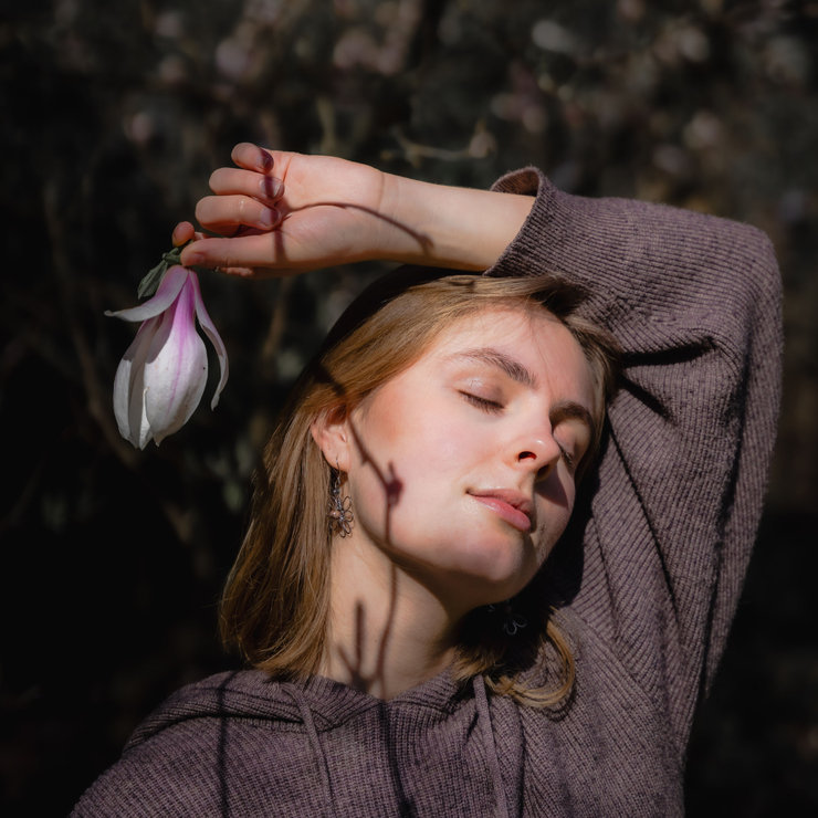 Een vrouw die haar ogen gesloten heeft in een vredige blik en een magnolia bloem vasthoudt die een schaduw maakt op haar gezicht
